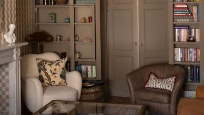 living room with custom shelving built round the door and painted in Farrow & Ball's Mouse's Back with two small armchairs and wallpapered walls