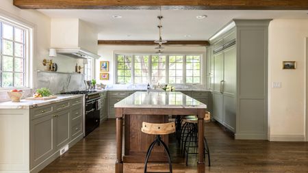 A U-shaped kitchen with cabinets painted in French Gray by Farrow and Ball, marble countertops, brass hardware, and a wooden island