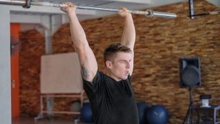 Man performs overhead press with empty Olympic barbell