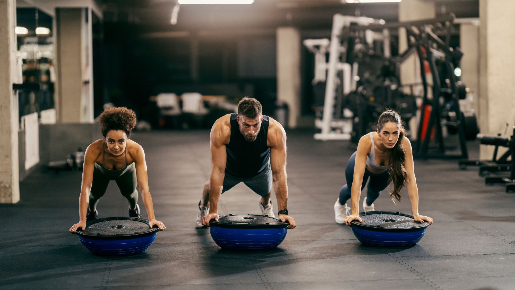 Three people doing bosu ball exercises in a gym