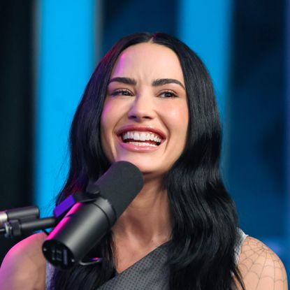 a white woman with long, dark hair laughing in front of microphone while speaking on a radio show