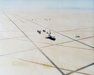This high angle view shows the scene at Edwards Air Force Base in southern California soon after the successful landing of the space shuttle orbiter Columbia to end STS-1. Service vehicles approach the spacecraft to perform evaluations for safety, egress
