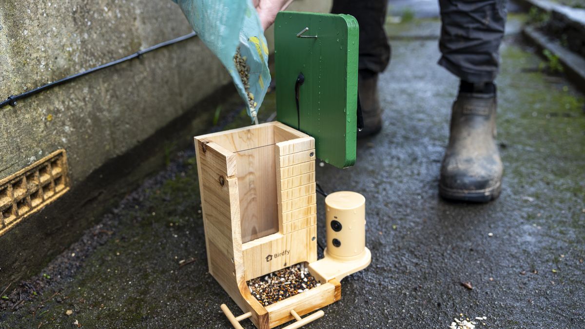 A male in wellies filling up the Birdfy Wood feeder with seed