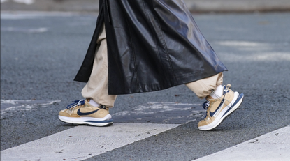  A passerby wears a black shiny leather belted long trench coat, beige cargo pants, beige nylon and burgundy logo sneakers from Nike , during a street style fashion photo session, on April 15, 2023 in Paris, France. (