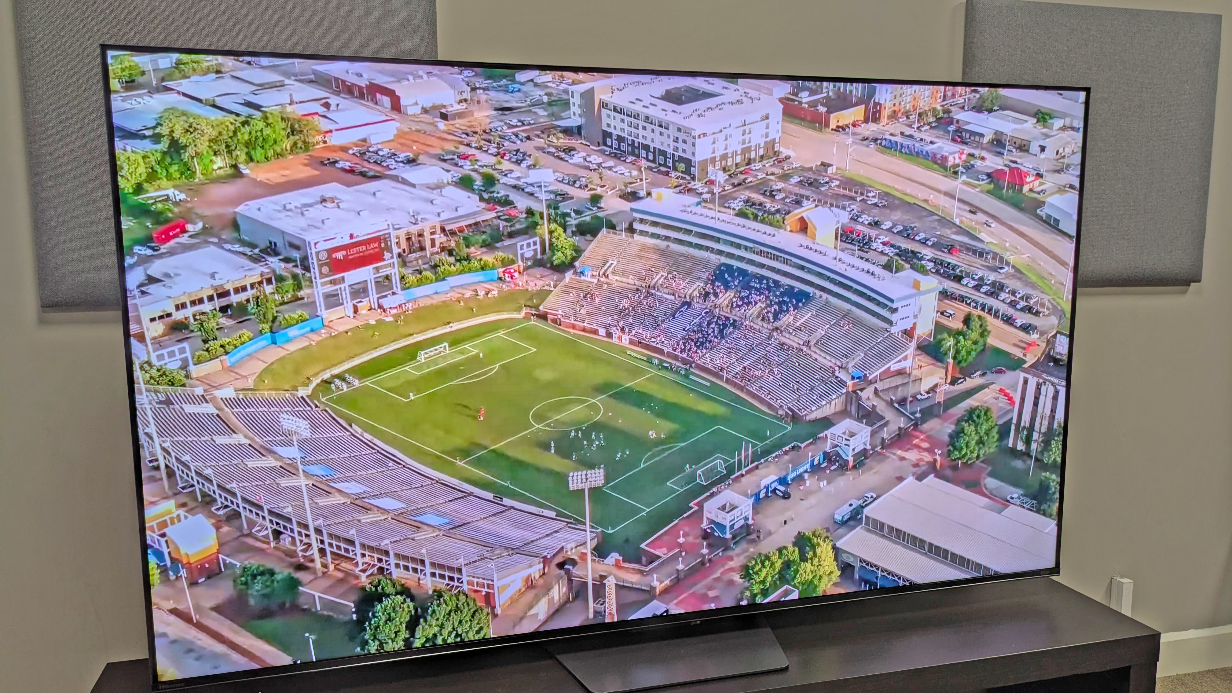 Hisense U7S Pro TV with an aerial shot of an outdoor football stadium in the day on screen, with photo taken from left angle