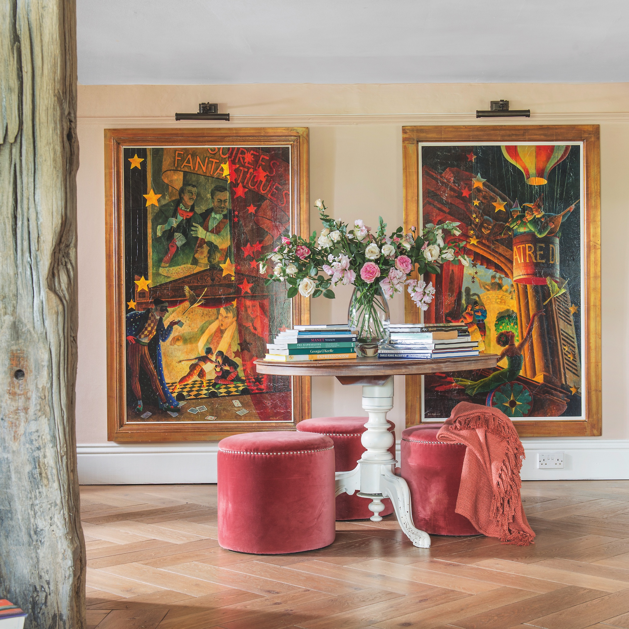 large reception hall in 18th century house with circular table and velvet stools with large artworks on wall