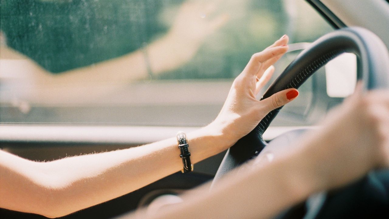 A woman&#039;s hands on a car steering wheel.