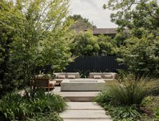 A garden with green plants, a paved path, and a recessed seating area with outdoor furniture