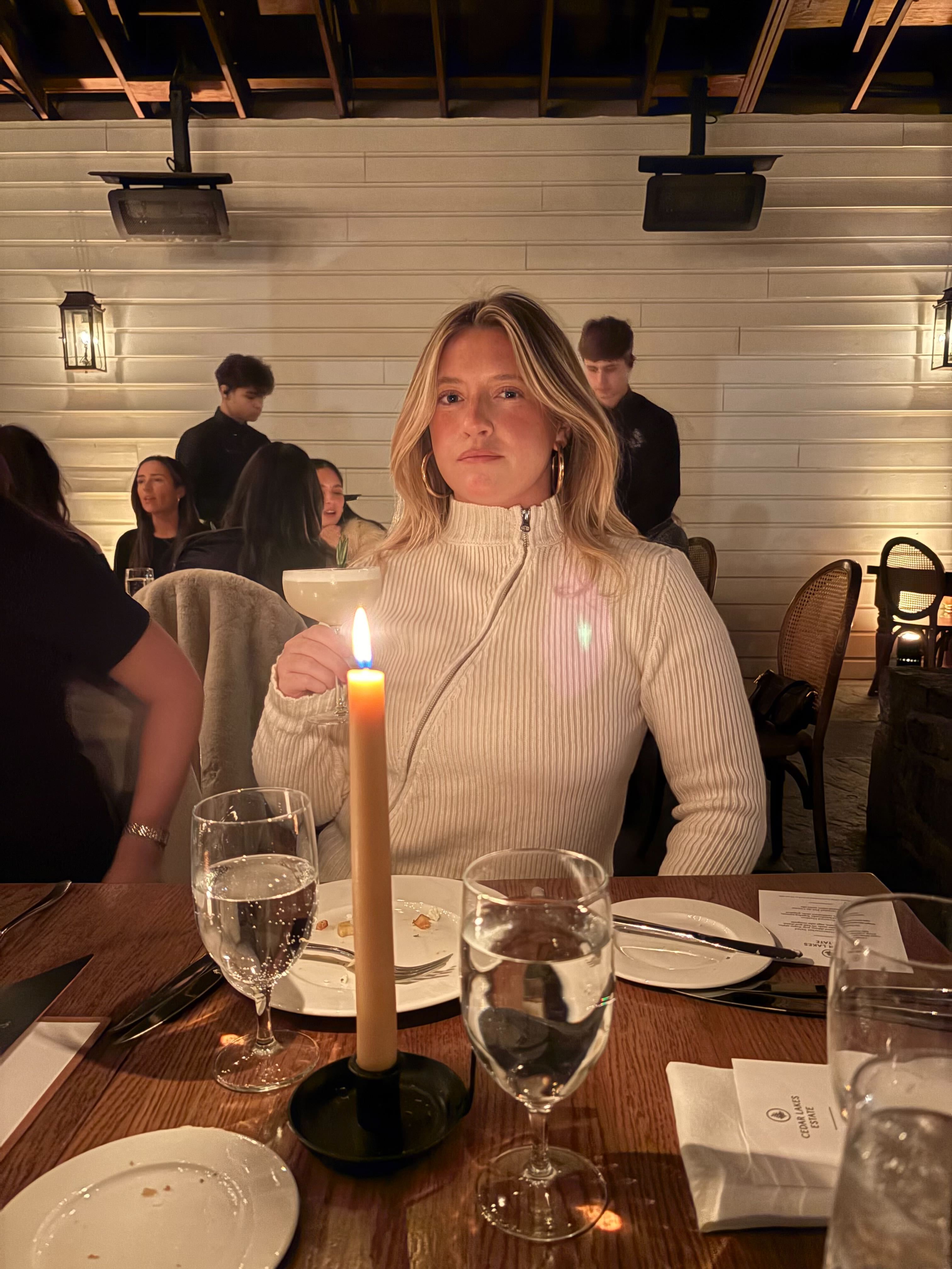 NewYork City fashion and beauty influencer Martine Lavelle poses with a cocktail at a chic restaurant wearing a Gimaguas zip-up mock neck sweater