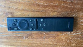 The remote control for the Samsung QE55Q60B TV pictured on a wooden surface.