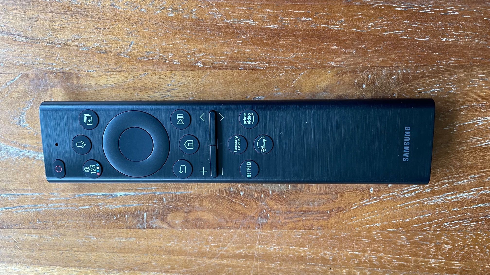 The remote control for the Samsung QE55Q60B TV pictured on a wooden surface.