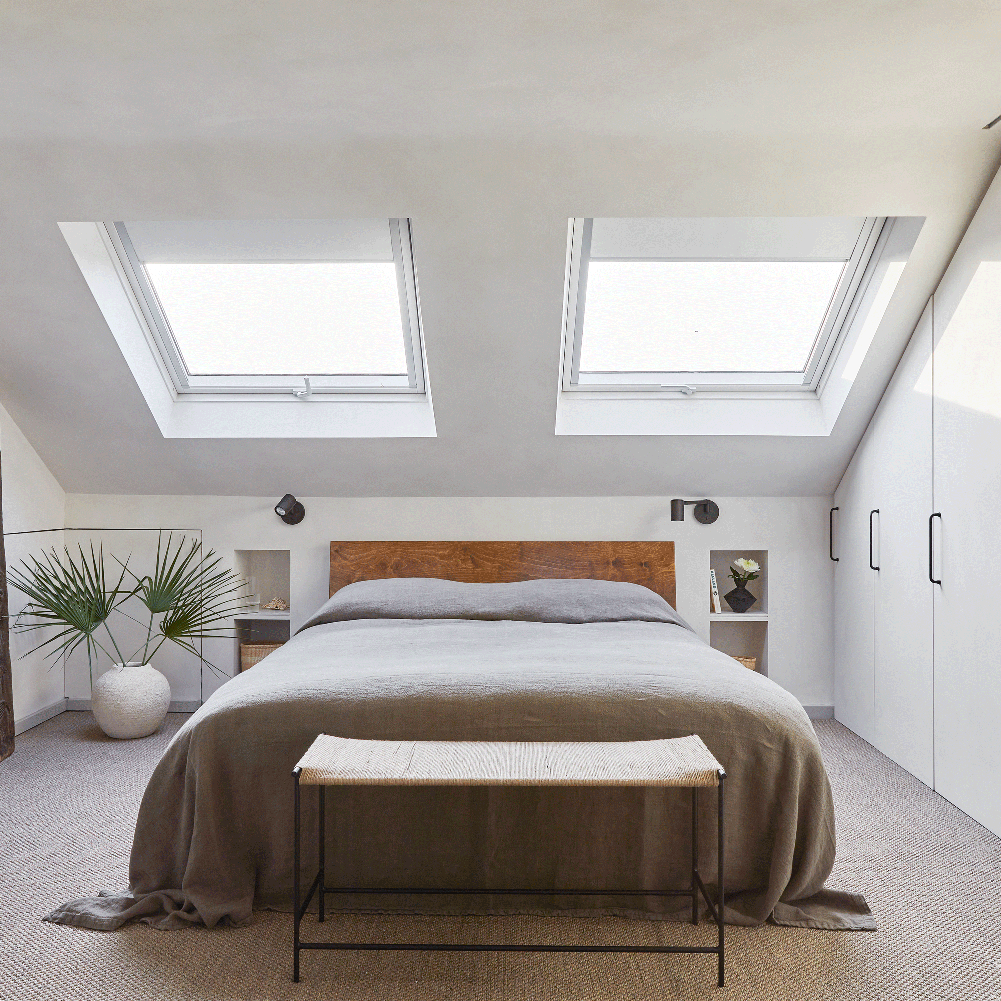 a white loft bedroom with two large roof windows above a large double bed and built in furniture in the eaves