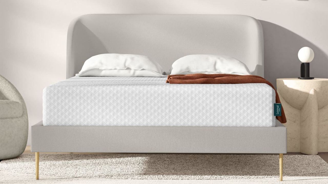 Leesa Sapira Hybrid Mattress on a bed with pillows and a blanket against a white wall.