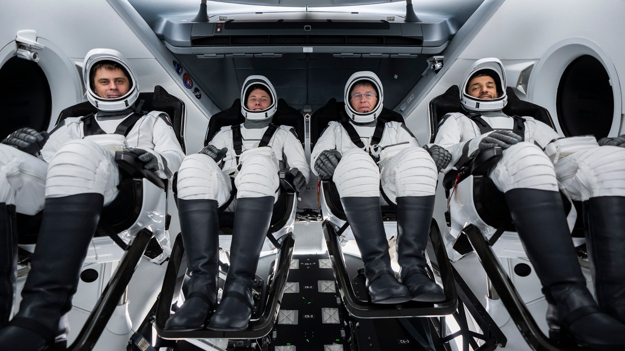 Cuatro astronautas sentados en una tripulación de dragones con trajes espaciales y cinturones de seguridad