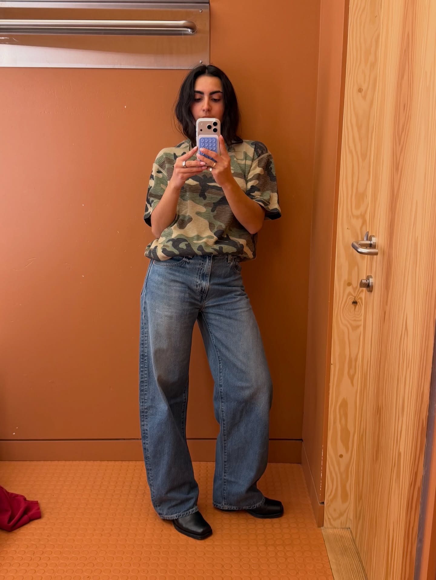 Influencer Chloe Mihailovich wearing a camo print t-shirt, barrel-leg jeans and square toe boots.