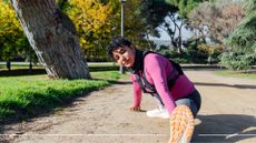 Woman stretching into sideways squat in weighted vest workout outdoors in sunshine wearing trainers and workout clothes