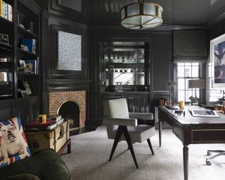 A library with black walls, brick fireplace and a desk