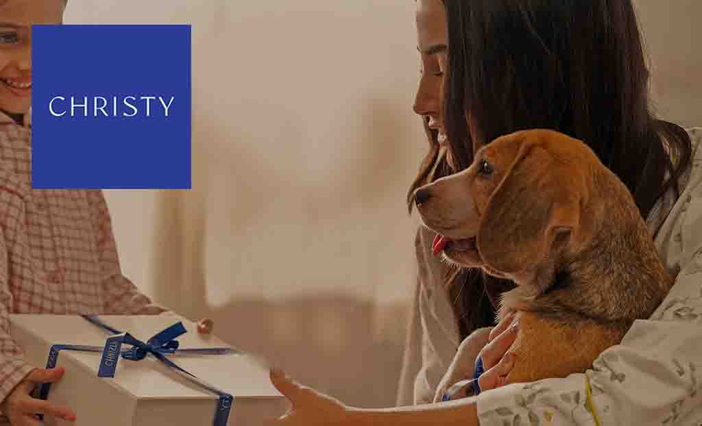 Christy logo placed over an image of a son gifting his mum whilst she holds a beagle