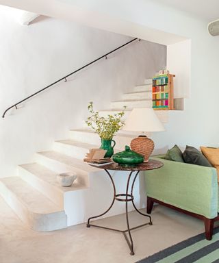 white stairs in living room with green sofa, small round occasional table and colorful crate i