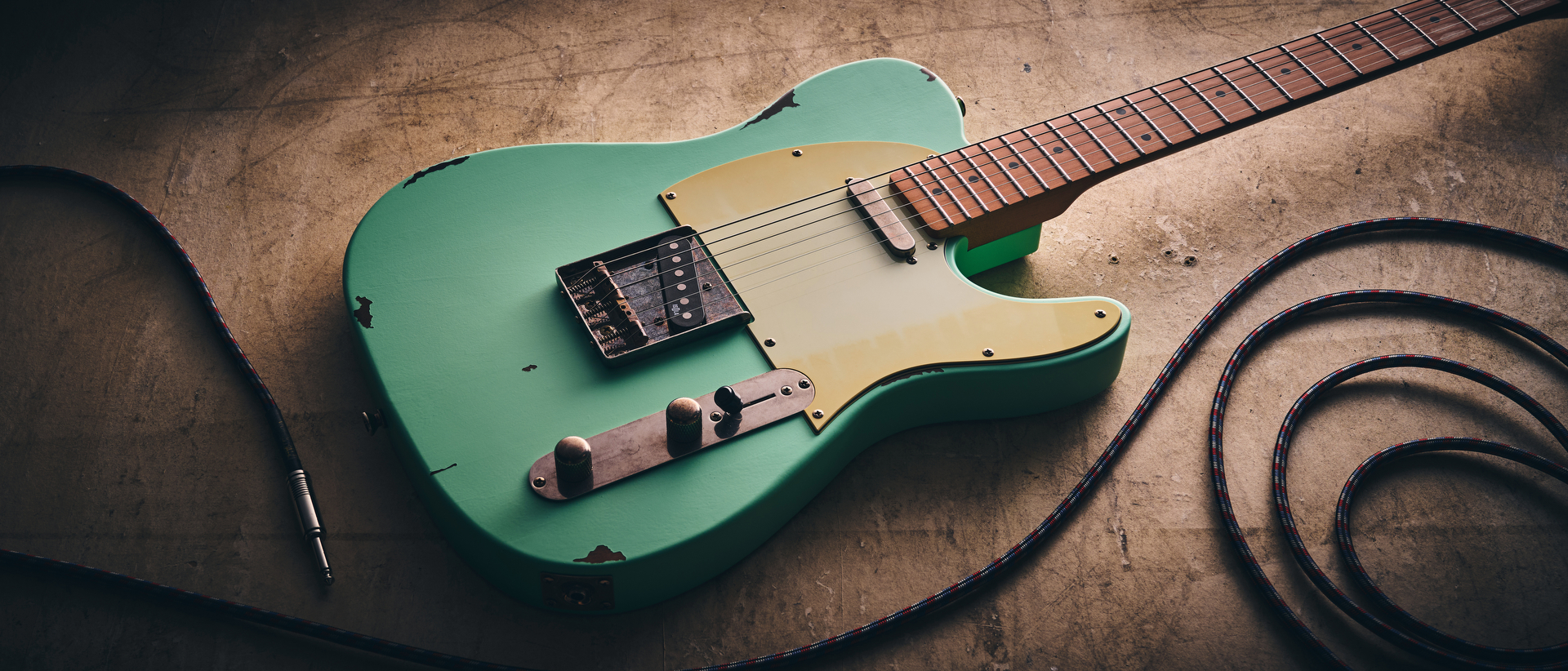 A Harley Benton TE-62LA electric guitar on a distressed concrete floor with a guitar cable