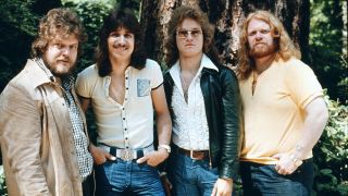A photograph of Bachman-Turner Overdrive posing outside in a forest, circa 1975