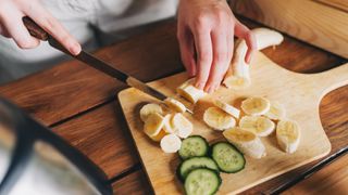Woman's hands chopping a banana on wooden chopping with slices of cucumber