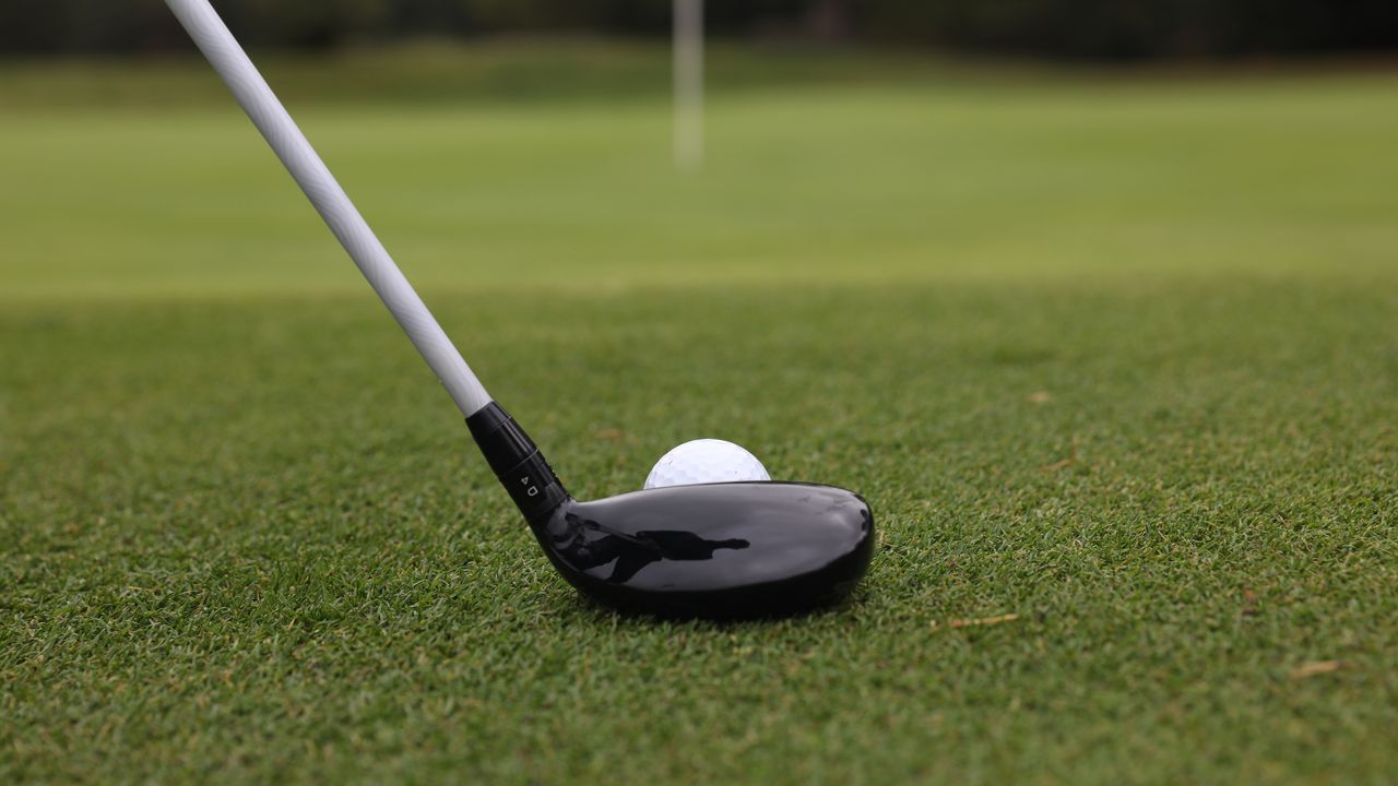 A golfer about to hit a chip with a hybrid golf club