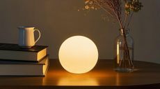 Orb lamp sitting on wooden table next to a clear vase and a stack of books