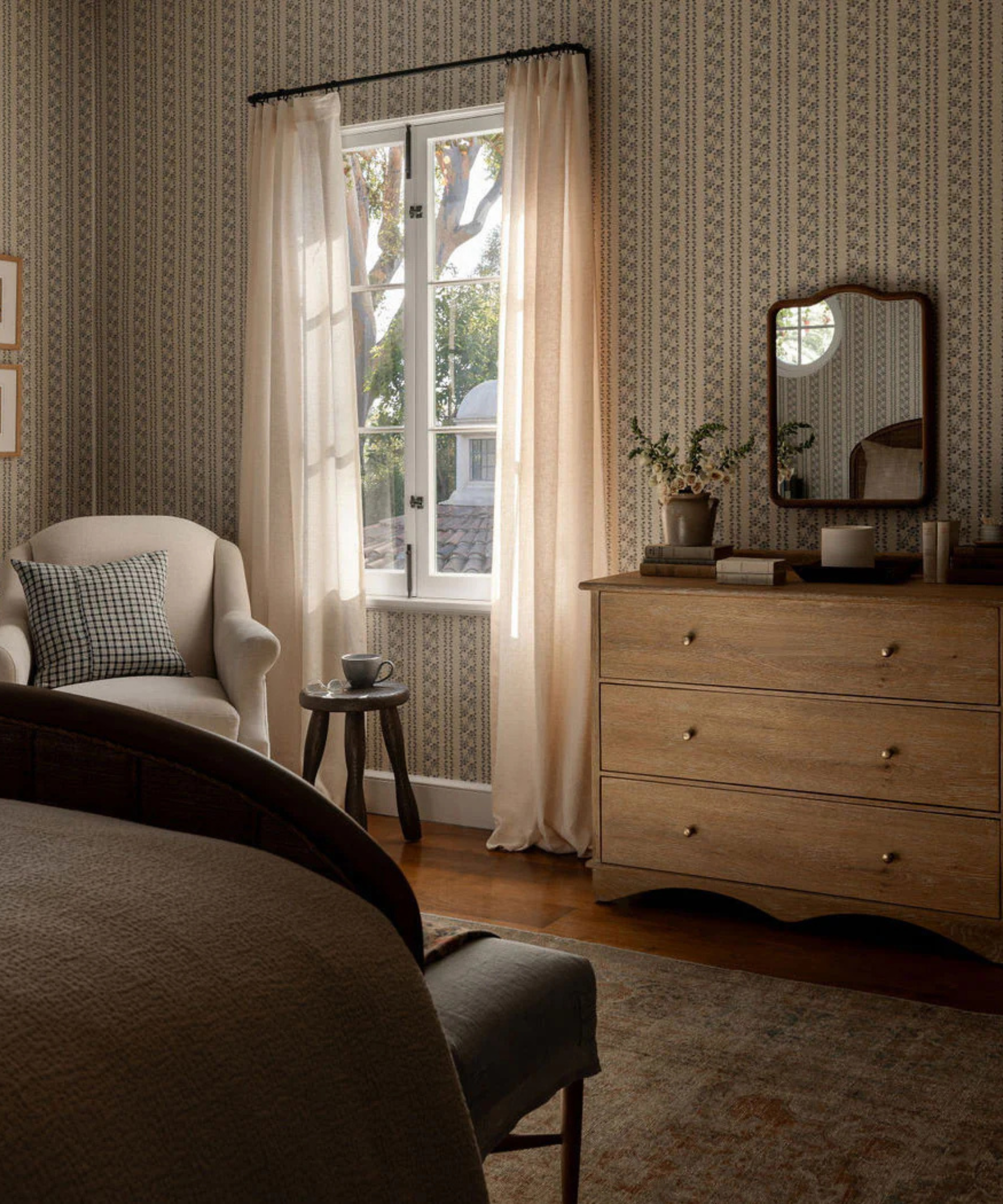 a bedroom with a wood dresser, a small mirror, and a large window with curtains