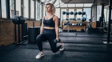 Woman in gym lunging while holding dumbbells