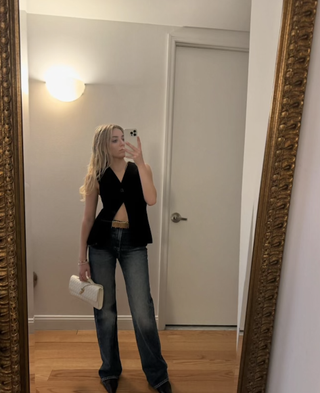 Zoe Gofman wearing dark-wash jeans, a black top, a tan belt, and a white Andiamo clutch from Bottega Veneta.