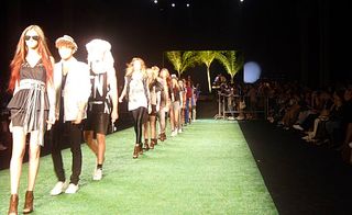 A line of models walking down a runway with the band in the background
