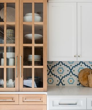 A white kitchen with white and blue patterned tiles, white cabinets and single wooden glass-fronted cabinet