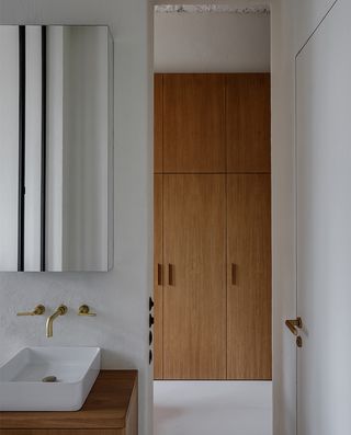 A bathroom with a wooden vanity, a white sink, a mirror and a wooden cupboard.