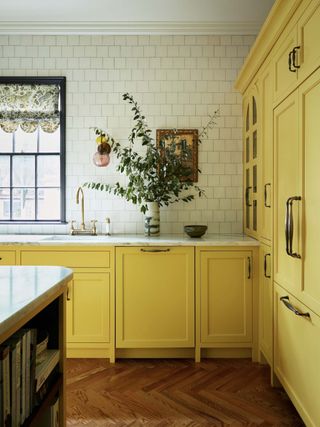 yellow kitchen with parquetry floors, marble countertop, white tiled backsplash, and brass handles