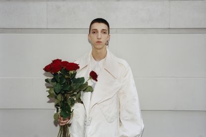 Man in Simone Rocha menswear white jacket holding flowers against wall