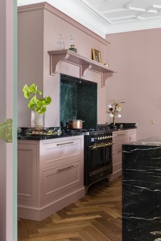pink kitchen with jade marble backsplash, herringbone floor, black marble island and countertops, range cooker