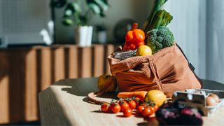 Bag of fruits and vegetables sitting on wooden table in kitchen in the sunshine