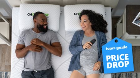A bird's eye view of a man and woman lying on a GhostBed Massage Foam Mattress. In the bottom right, a Tom's Guide Price Drop deals graphic