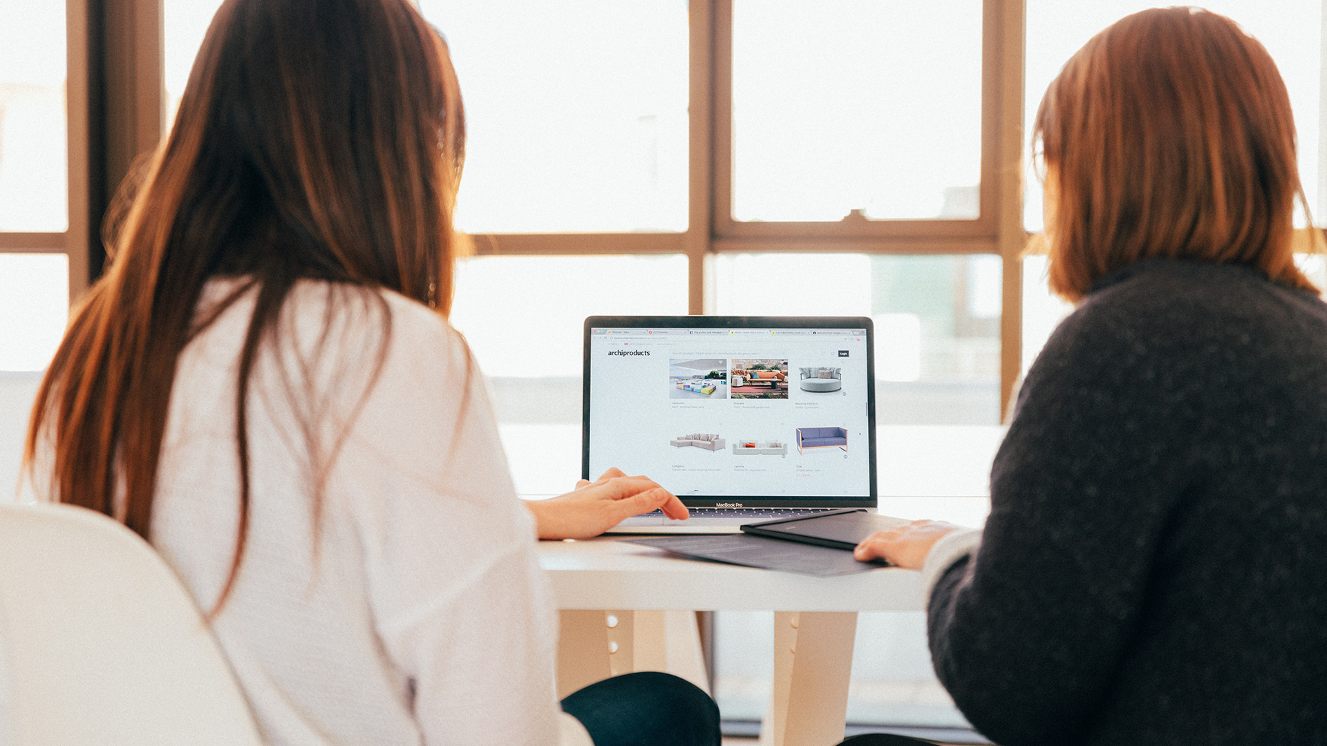 two women sat at desk looking at laptop displaying website