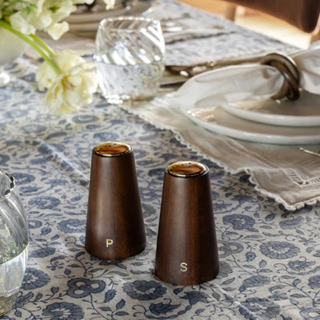 Wooden salt and pepper shakers on a dining table covered in blue and white tablecloth.