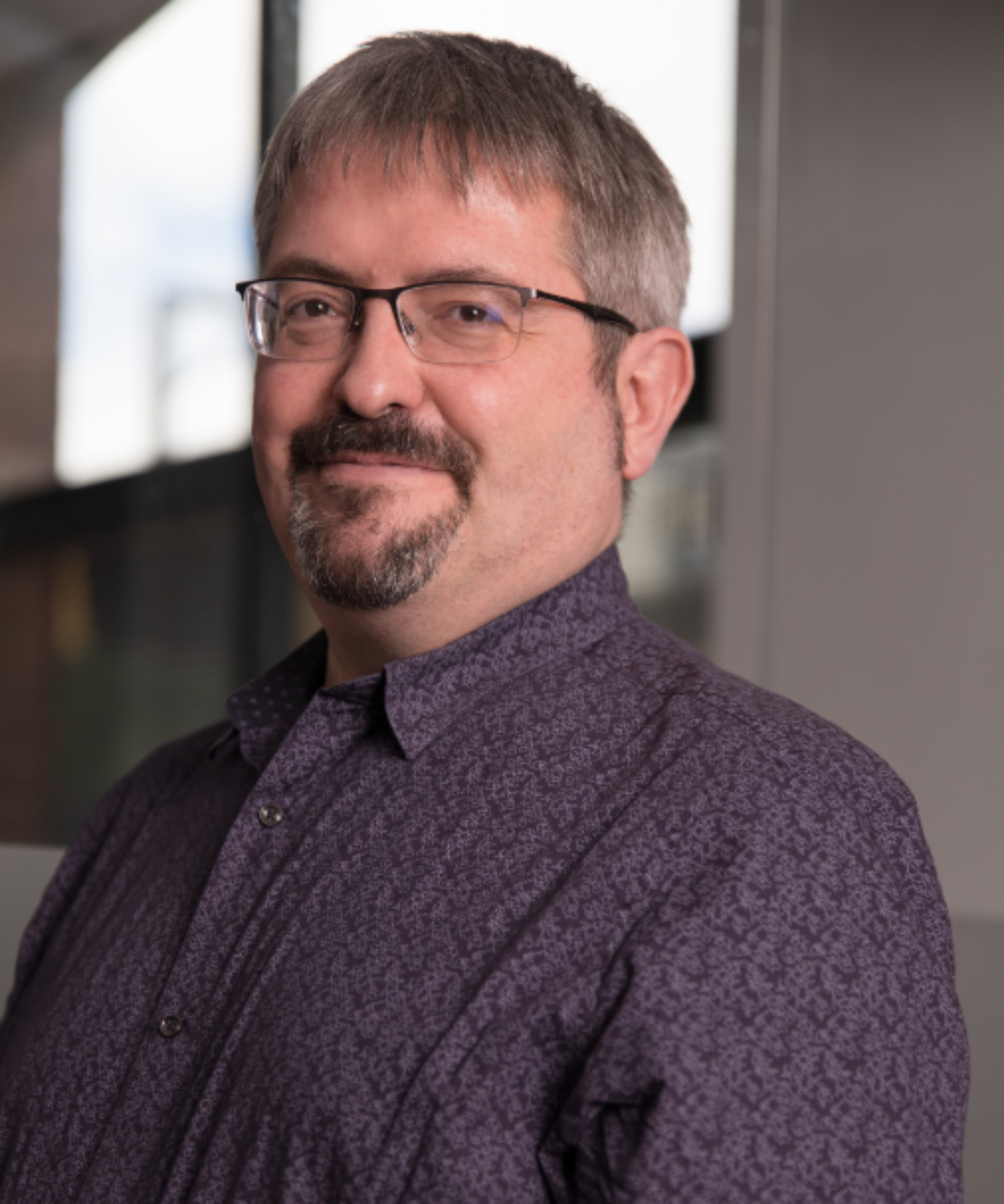 male with glasses, grey hear, short beard wearing dark purple shirt