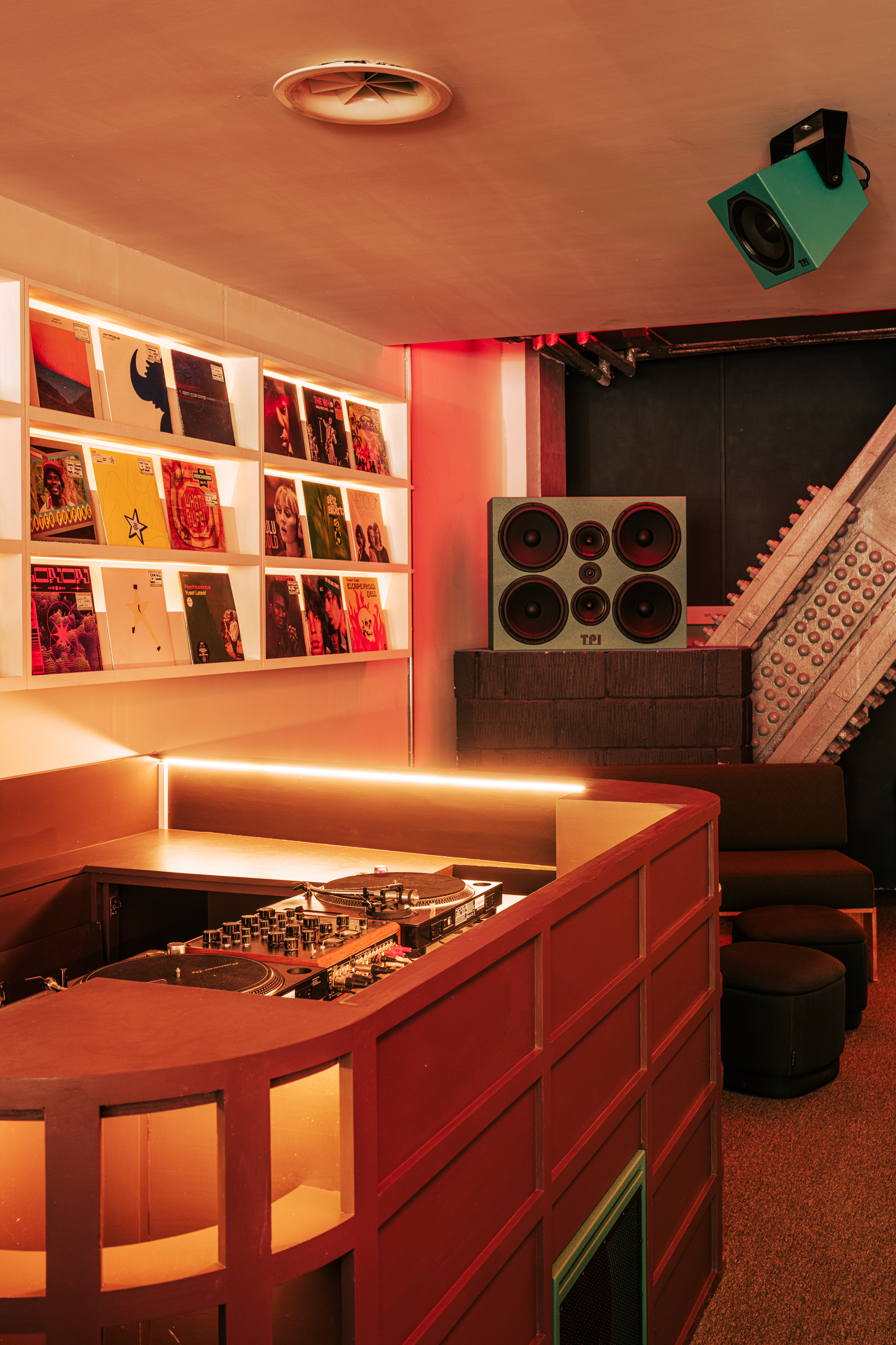 A red neon-lit listening bar packed with retro-fueled furnishings, geometrical lines, functional equipment, and an immersive vibe.