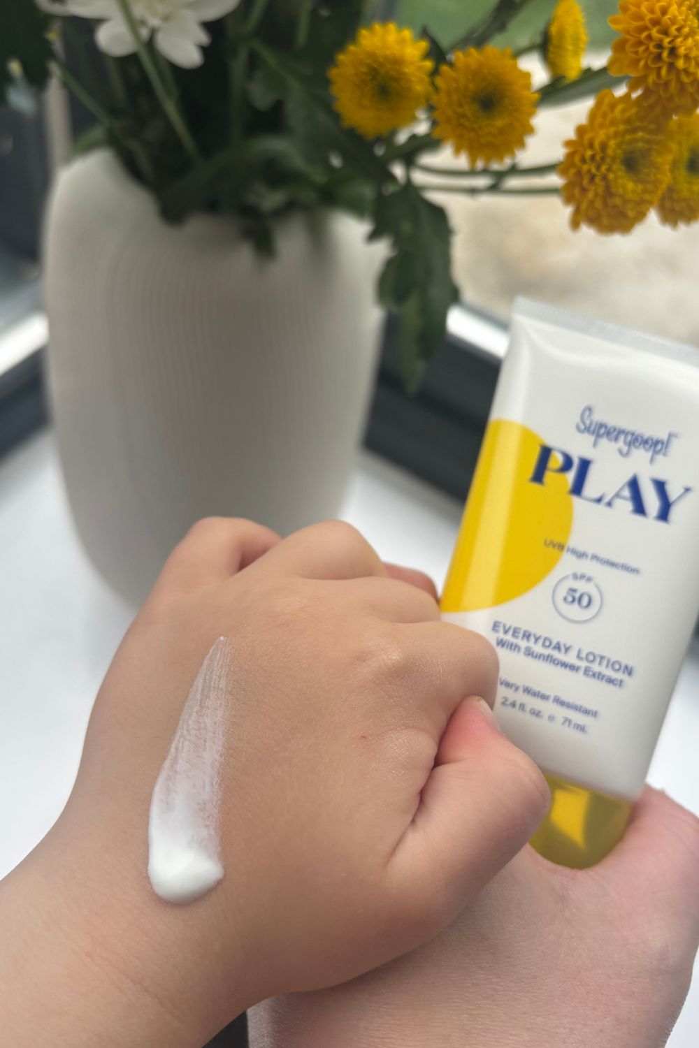 a childs hand holding matilda's hand with a smear of supergoop play lotion