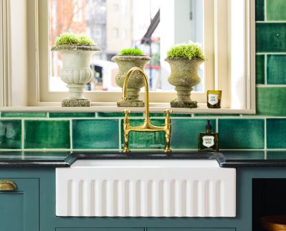 An aged brass faucet with a farmhouse sink and green tiles