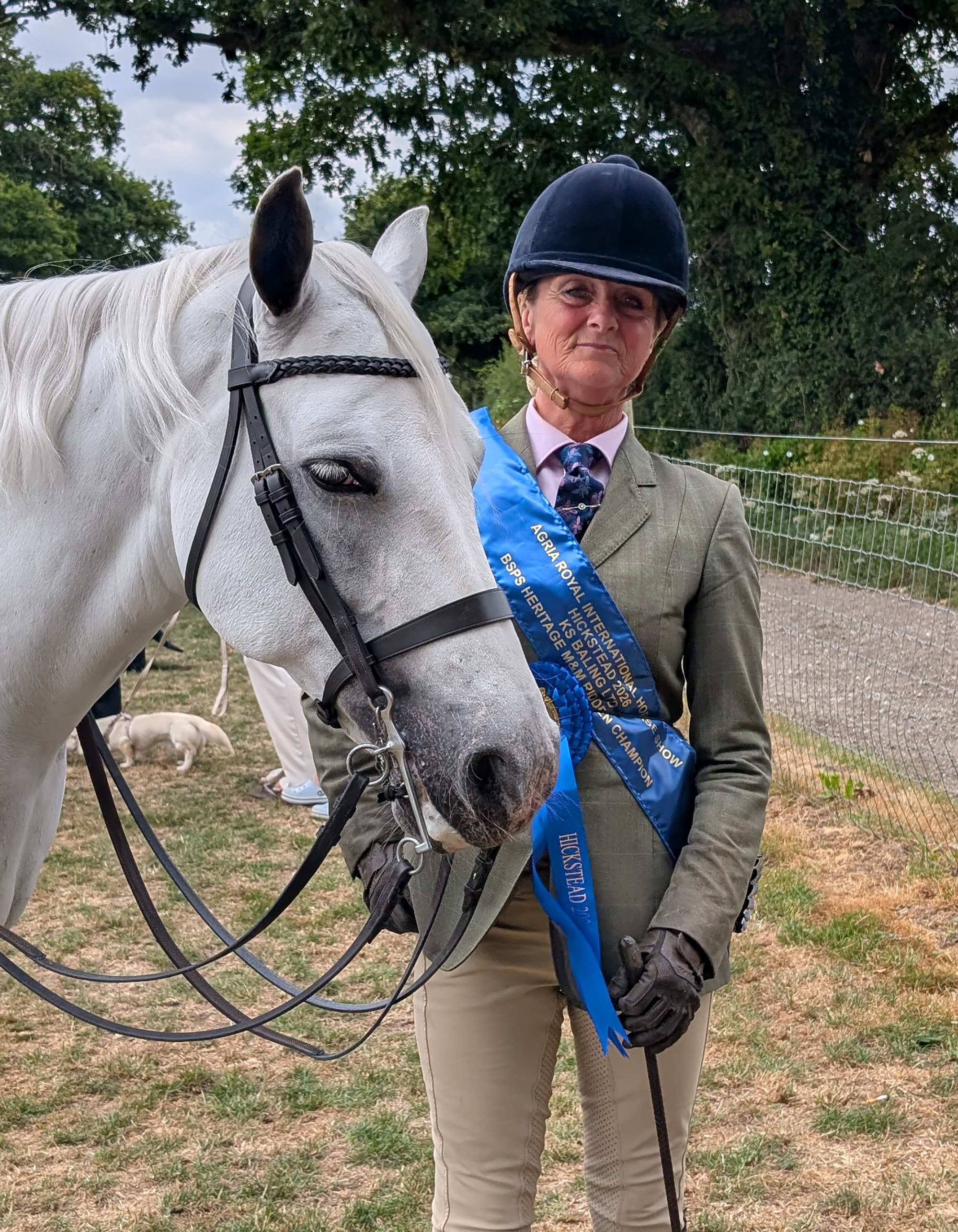 A grey Connemara with rider standing alongside wearing the champions blue sach and winner&amp;AElig;s rosette