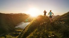 Man and woman running over hills at sunset as part of a trail running training plan