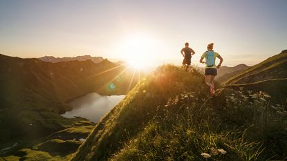 Man and woman running over hills at sunset as part of a trail running training plan