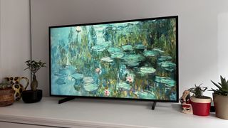 Et Samsung The Frame TV 2021 står på en hvid tv-bænk og viser et oliemaleri af åkander som baggrundsbillede.