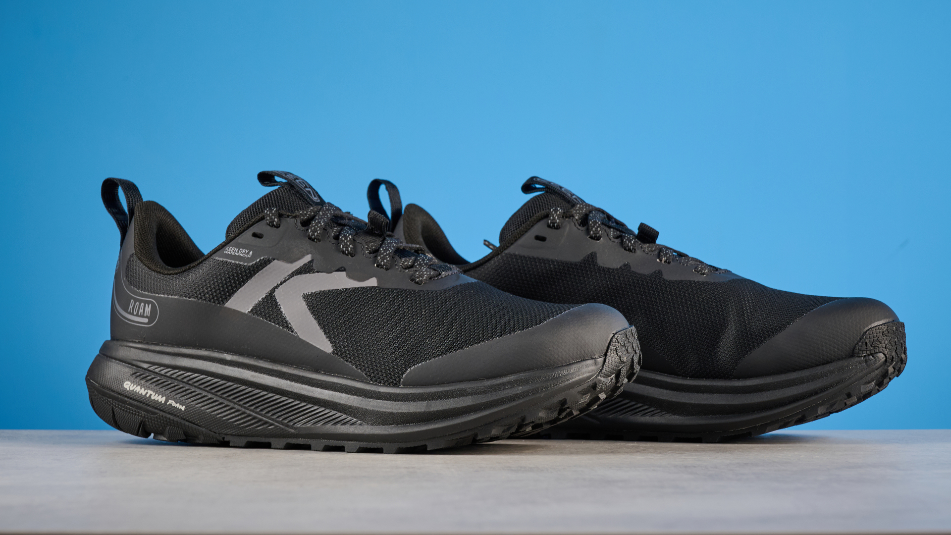 Keen Roam train running shoes in black photographed in front of a blue background